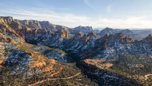 Aerial view of Sedona in winter with snow-dusted red rock formations and green pine trees under a clear blue sky